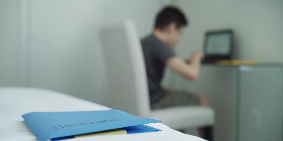 A child plays on his laptop while his homework sits on a table