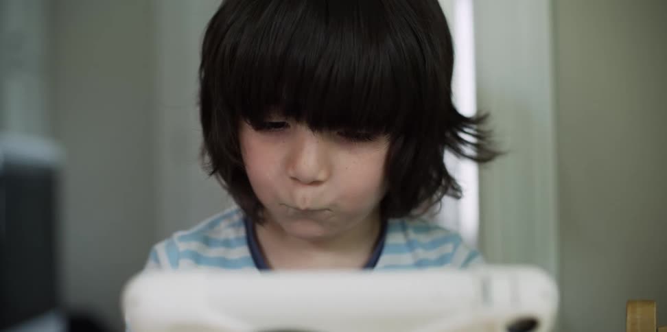 Boy in striped blue shirt sits watching tablet