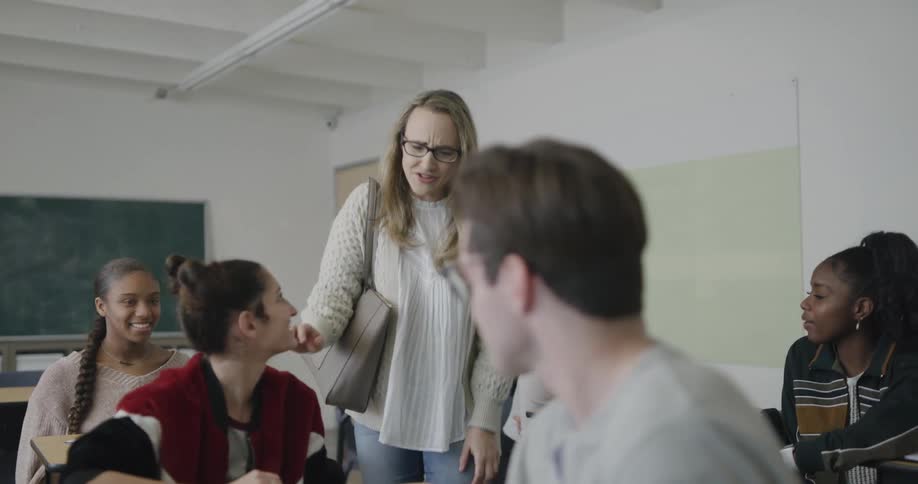 Students sitting in a classroom while the teacher walks in and talks to a student