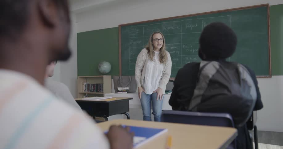 A teacher stands at the front of a classroom and instructs a high school class