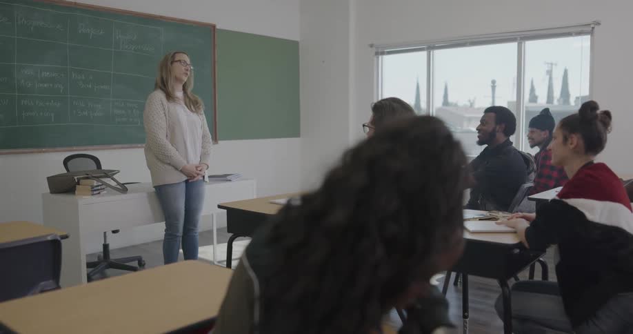 A group of students talk in class until their teacher walks in and starts talking to them