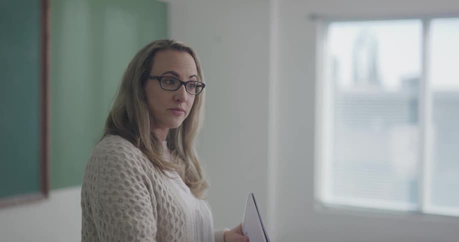 A teacher stands at the front of her classroom and talks