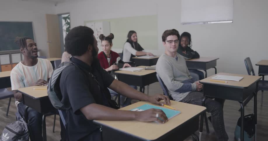 Students raise their hands as a teacher talks to them