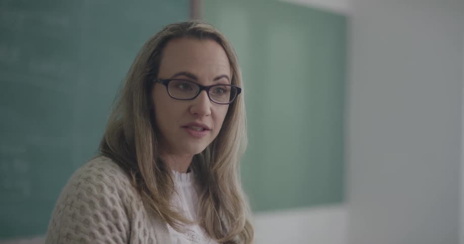 A teacher stands and talks in front of a chalkboard
