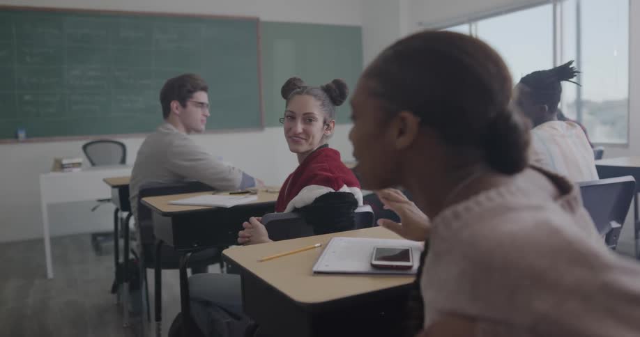 Two girls talk to each other in a classroom