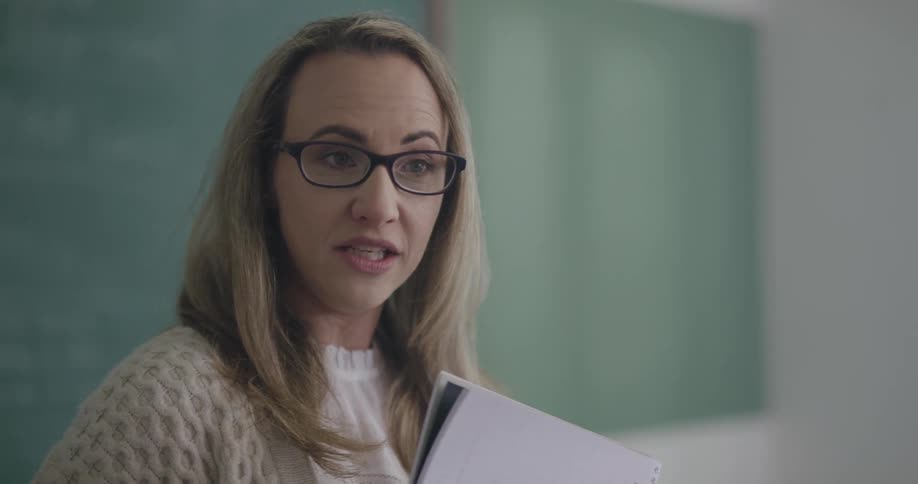 A teacher stands at the front of a class and talks