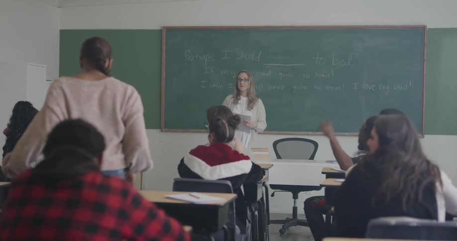 Students raise their hands to volunteer and the teacher selects a student to come to the front of the class