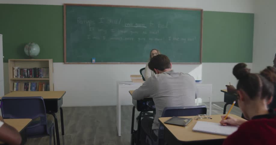 Students sitting in a classroom while the teacher sits at the front desk