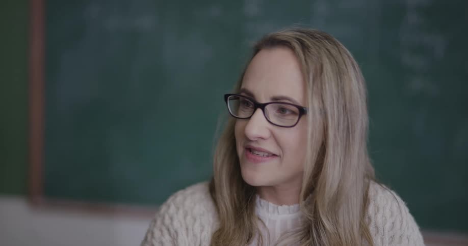 A teacher sits in front of a chalk board and talks