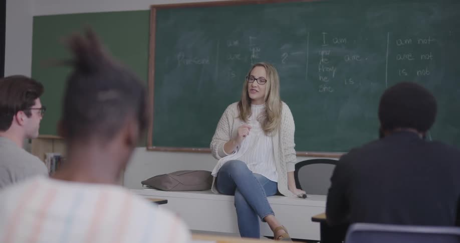 A teacher sits at the front of a classroom and talks to her students
