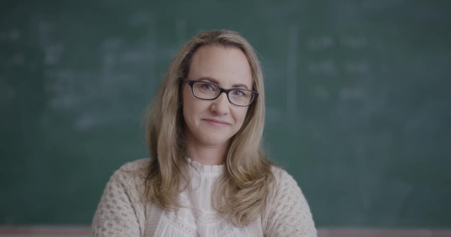 A teacher stands in front of a chalkboard in a classroom