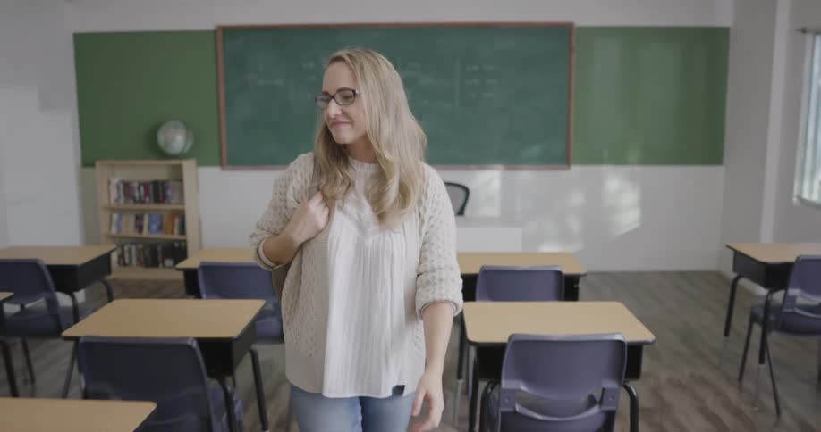 A teacher packs up her bag and walks out of her classroom