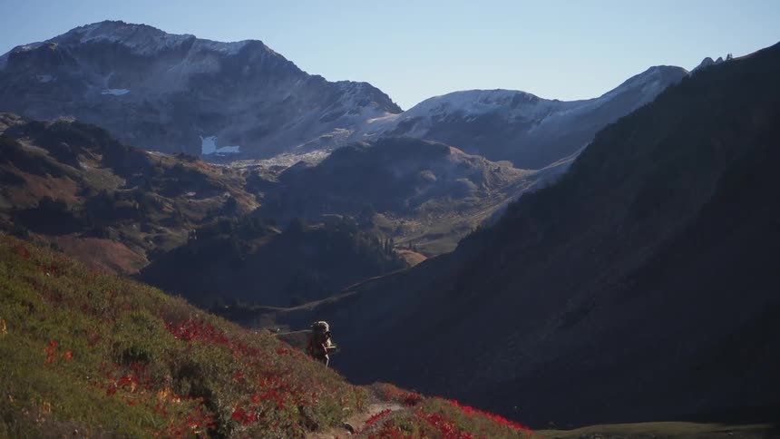 A person wearing a backpack hikes a hillside trail