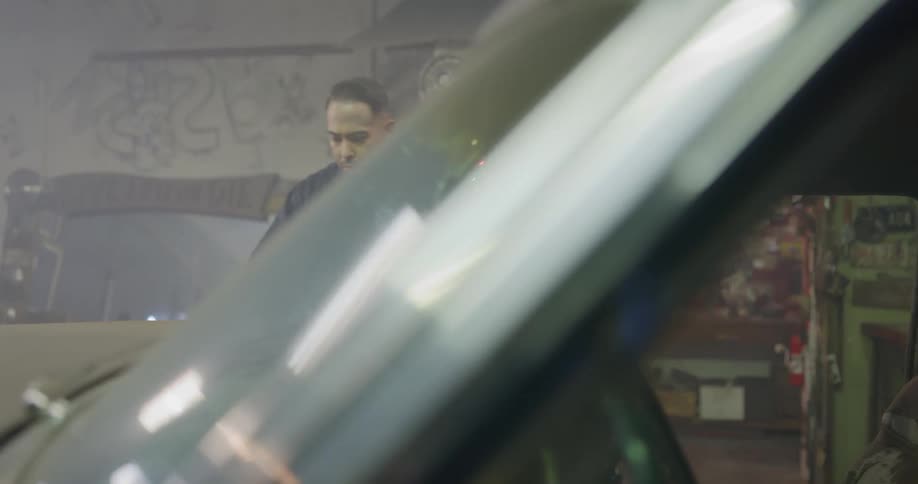 A mechanic opens a car door reaches in to pop the hood then braces it before starting to work on the engine