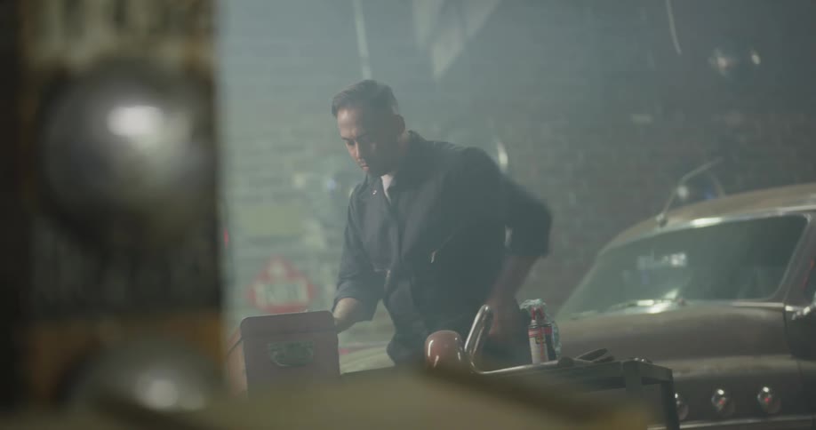 A mechanic walks past a classic car in his garage to put tools in a toolbox