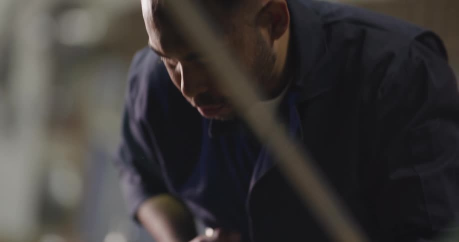 A mechanic holding a work light and a tool bends over to continue work on a car