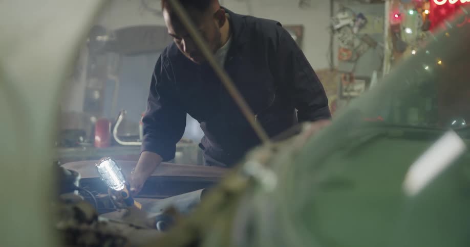 A mechanic shining a light underneath a car hood while working on a car