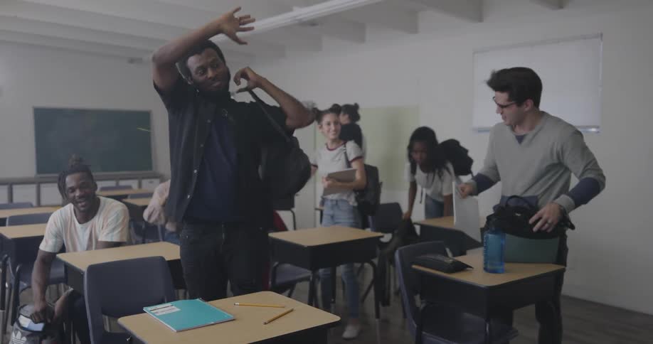 Students stand up and pack their things up at the end of class some waving to the teacher who follows them out the door