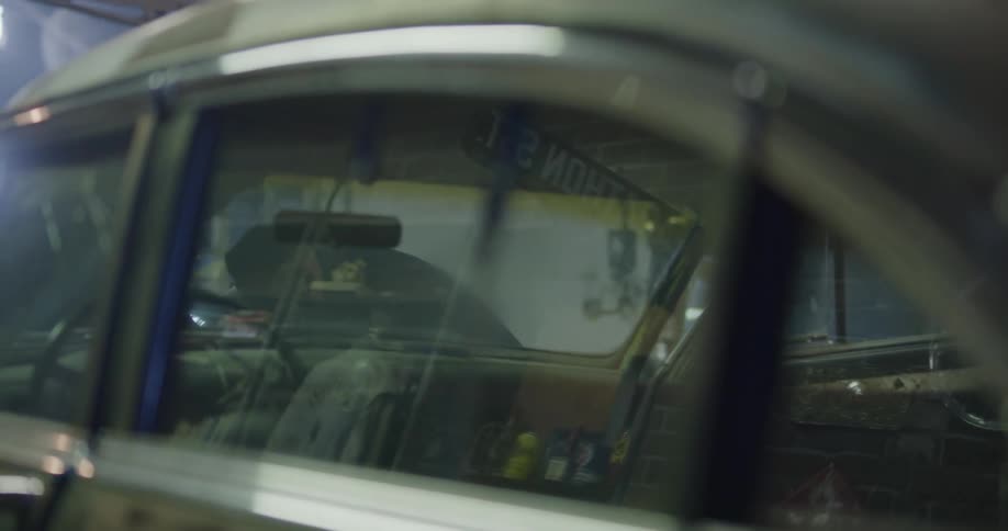 A mechanic looks under the hood of a car using a work light