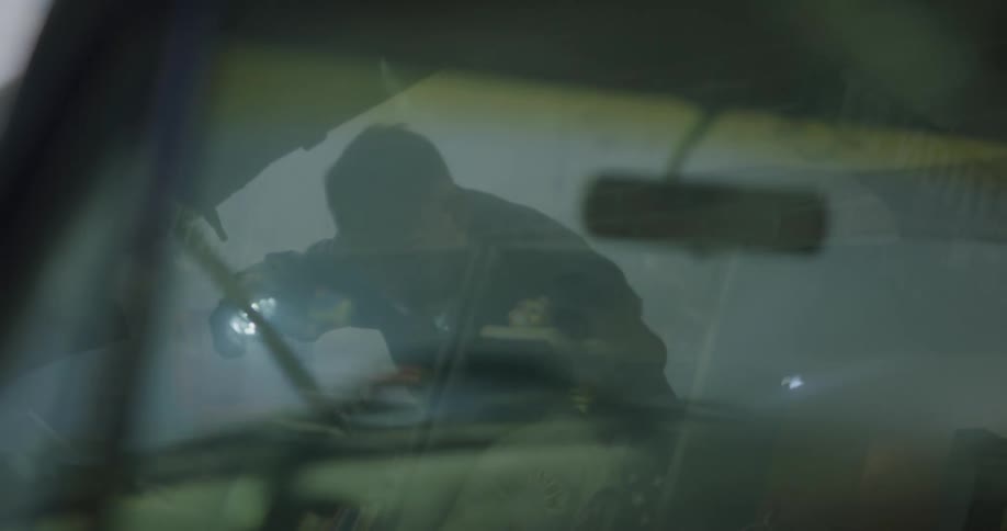 A mechanic working on a car shining a light under the hood