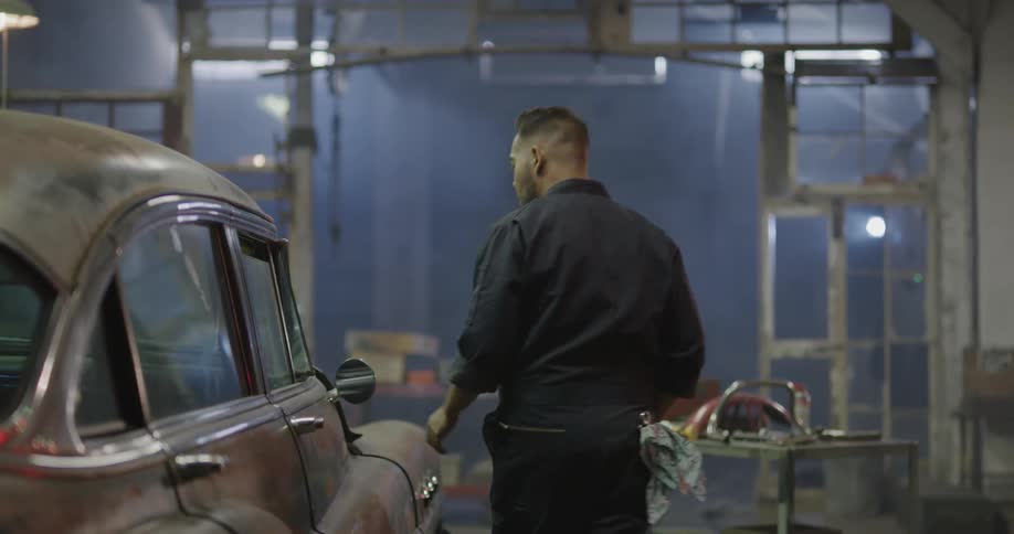 A mechanic in the garage opening up a car door and the car hood