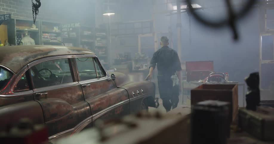 Mechanic walking by and patting vintage car in body shop