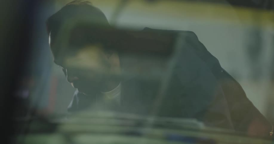 Mechanic working under a car hood at a body shop