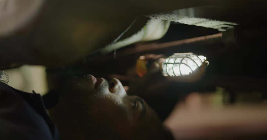 A mechanic looks at the undercarriage of a car with a light