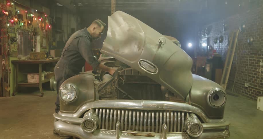 A mechanic looks under the hood of a broken down classic car
