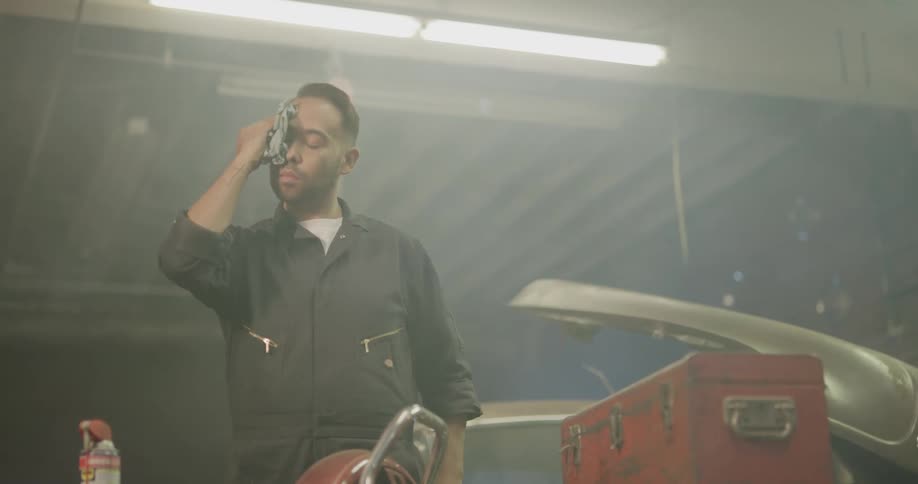 Car mechanic wipes hands and sweat before walking past car
