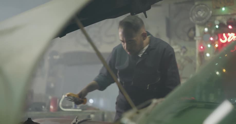 Car mechanic holds light in one hand while examining car engine