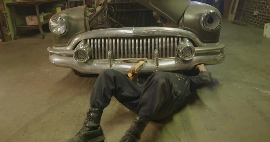 Car mechanic works on vintage cars engine and undercarriage