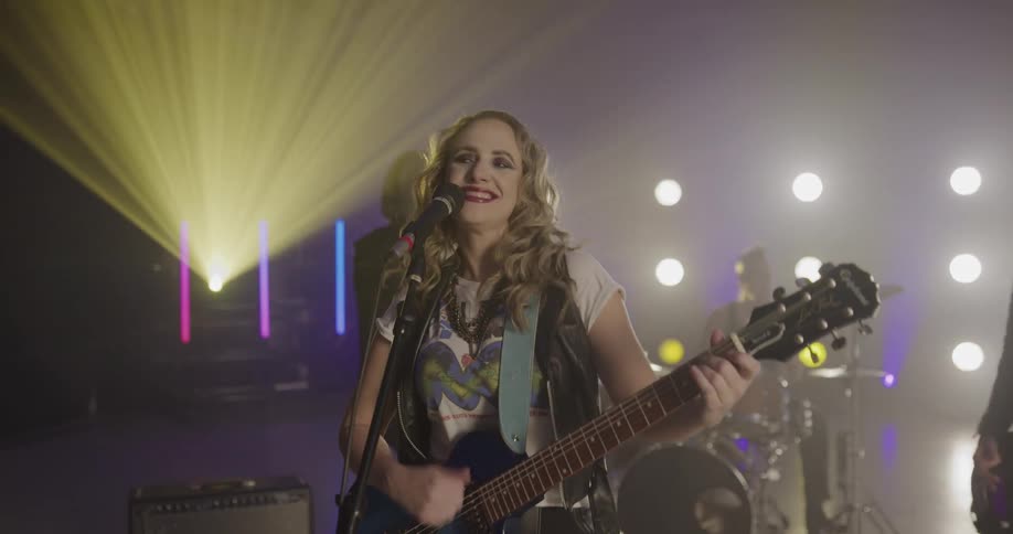 A female singing and playing the guitar on stage with a band