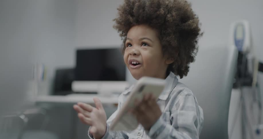 A young boy holds up a cell phone happily