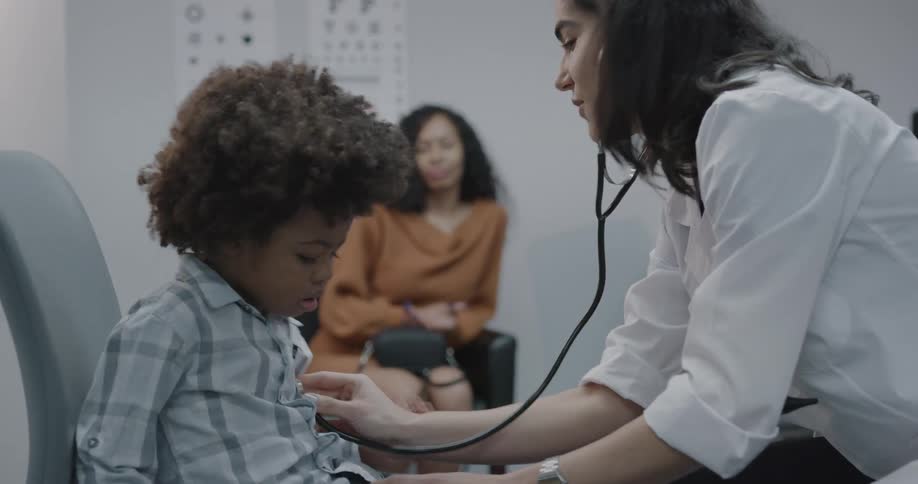 Doctor talks to mother as she examines patient with stethoscope