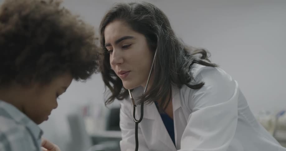 A female doctor listens to the heart and lungs of a toddler boy in a clinic office