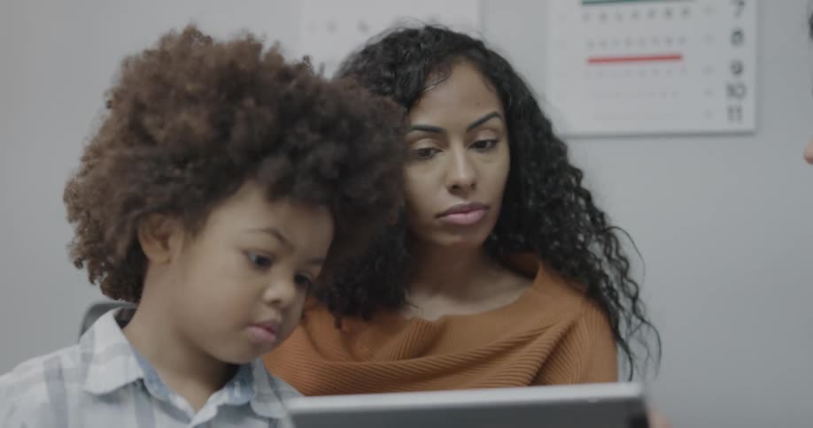 A doctor shows a mother and her son something on a tablet screen