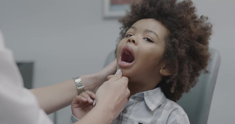 Doctor examines child mouth while the child sits