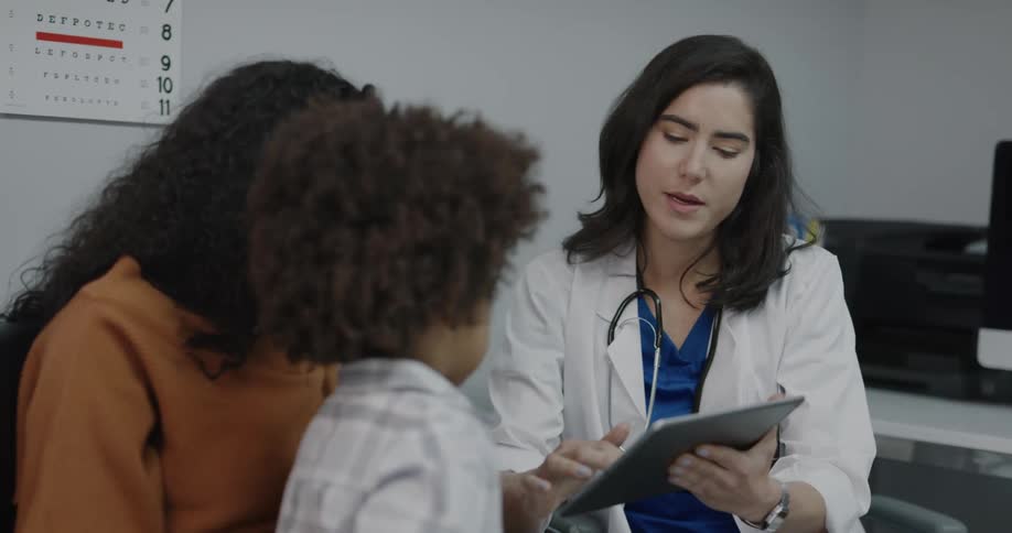 A doctor shows a tablet screen to a toddler patient and his mother