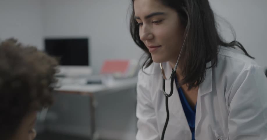 A doctor listens to a little boys chest with stethoscope as he takes a deep breath