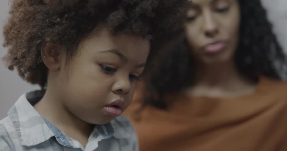 A mother sits with her son in a clinic as someone talks with him
