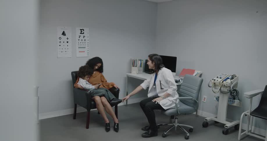 A doctor walks into a room to speak with her young patient and his mother