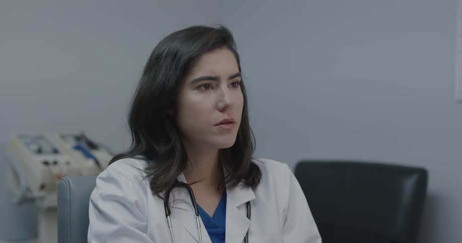 A doctor sitting in a chair looking at information then clasping her hands