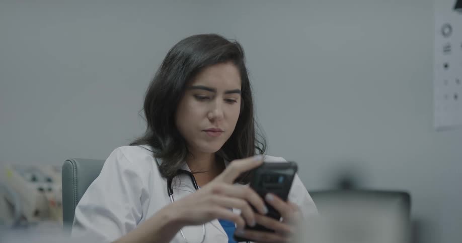 A doctor sitting in her office fiddles with her phone