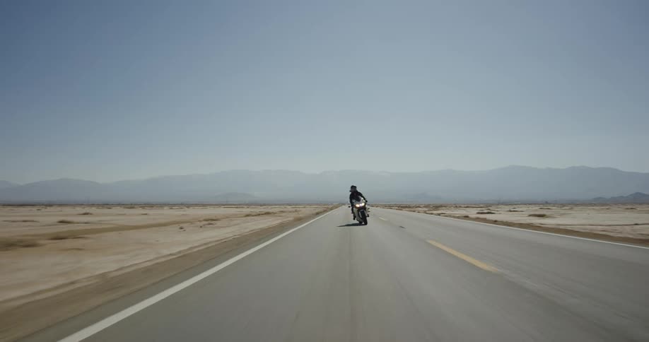 Woman rides motorcycle on a road through desert
