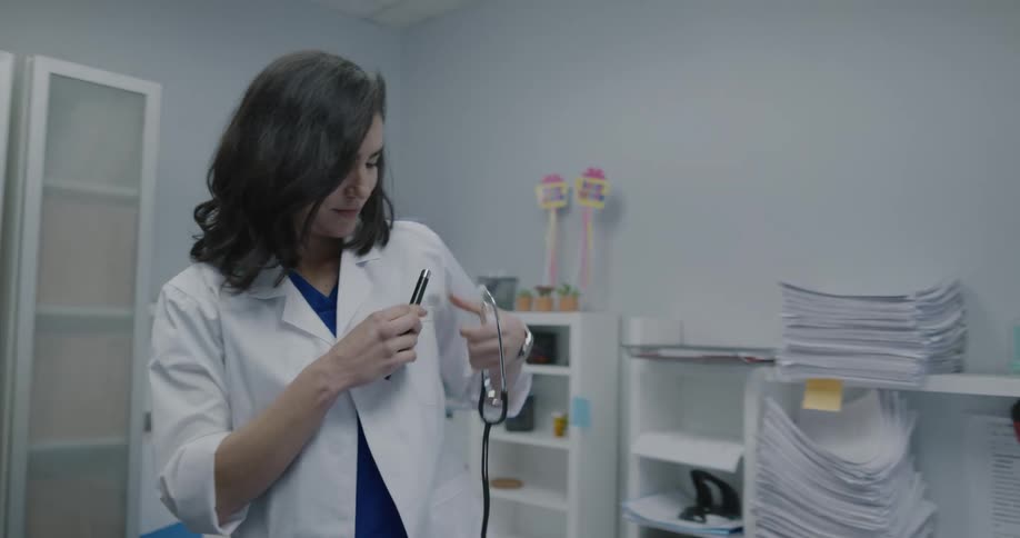A female doctor puts on her white coat and stethoscope and leaves the room