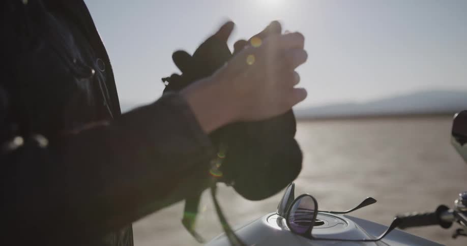 Woman on motorcycle takes off sunglasses gloves and helmet while parked in the desert