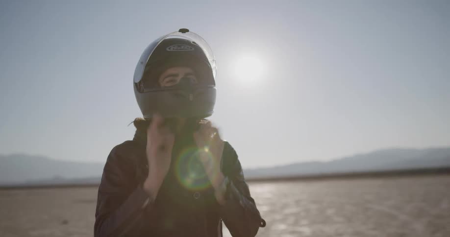 A motorcyclist takes off her helmet while parked in the desert