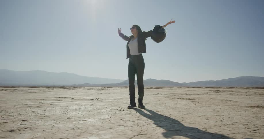 Woman with crash helmet on her elbow stands on the desert at day