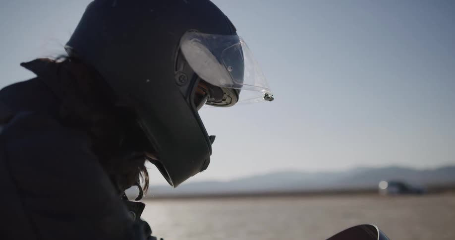 A female biker puts her gloves on while sitting on a dirt bike in the middle of the desert